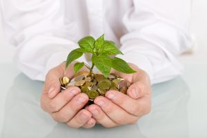 Business man holding young plant rising from a pile of coins - good investment and savings concept